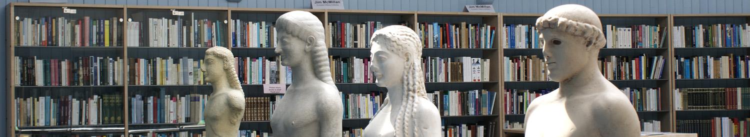 Four ancient statue heads sitting in front of a library bookcase