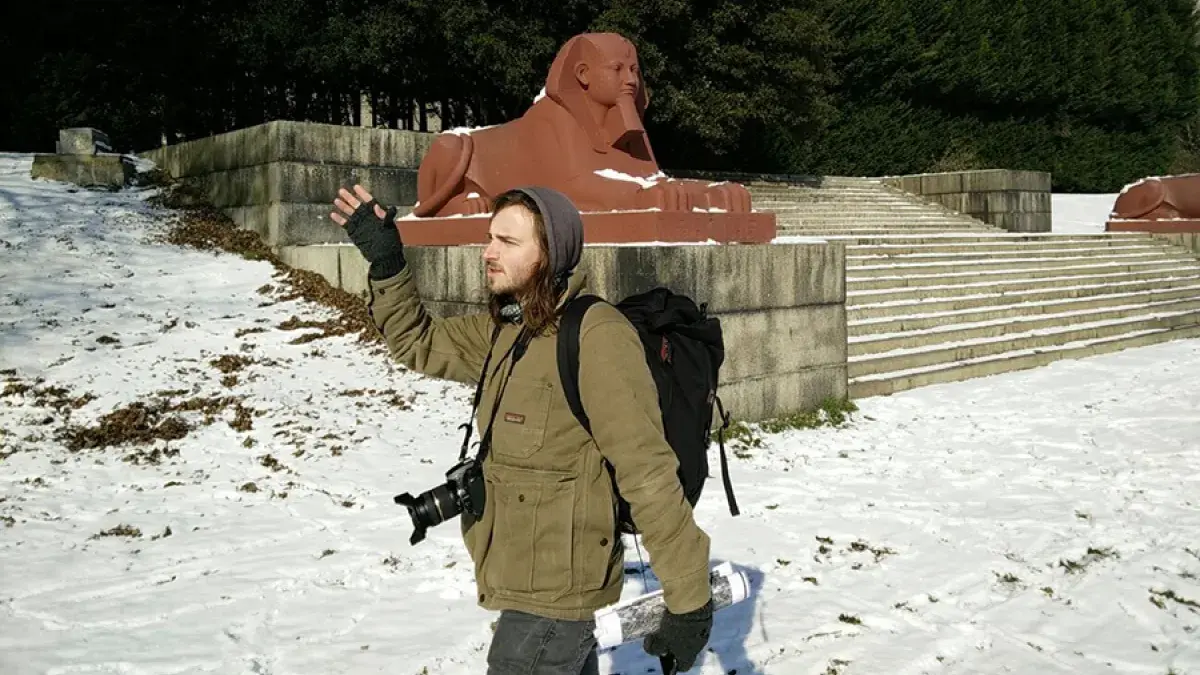Dr Jonathan Gardner standing near one of the entrances to the Crystal Palace during a snowy field trip, with a stone sphinx in the background.. 