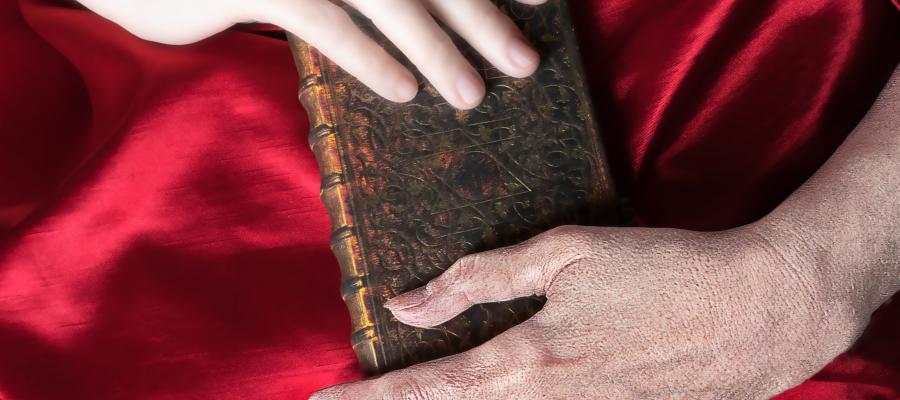 Against a red satin background, two hands - one young and one old - hold an old book.