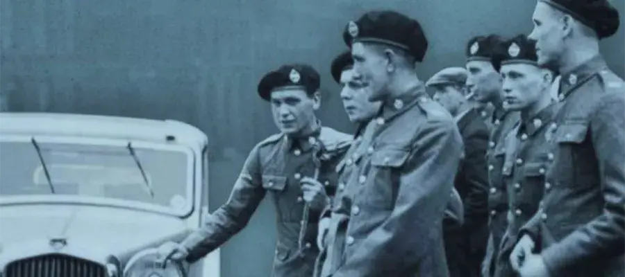 A group of young soldiers in berets stand beside a car