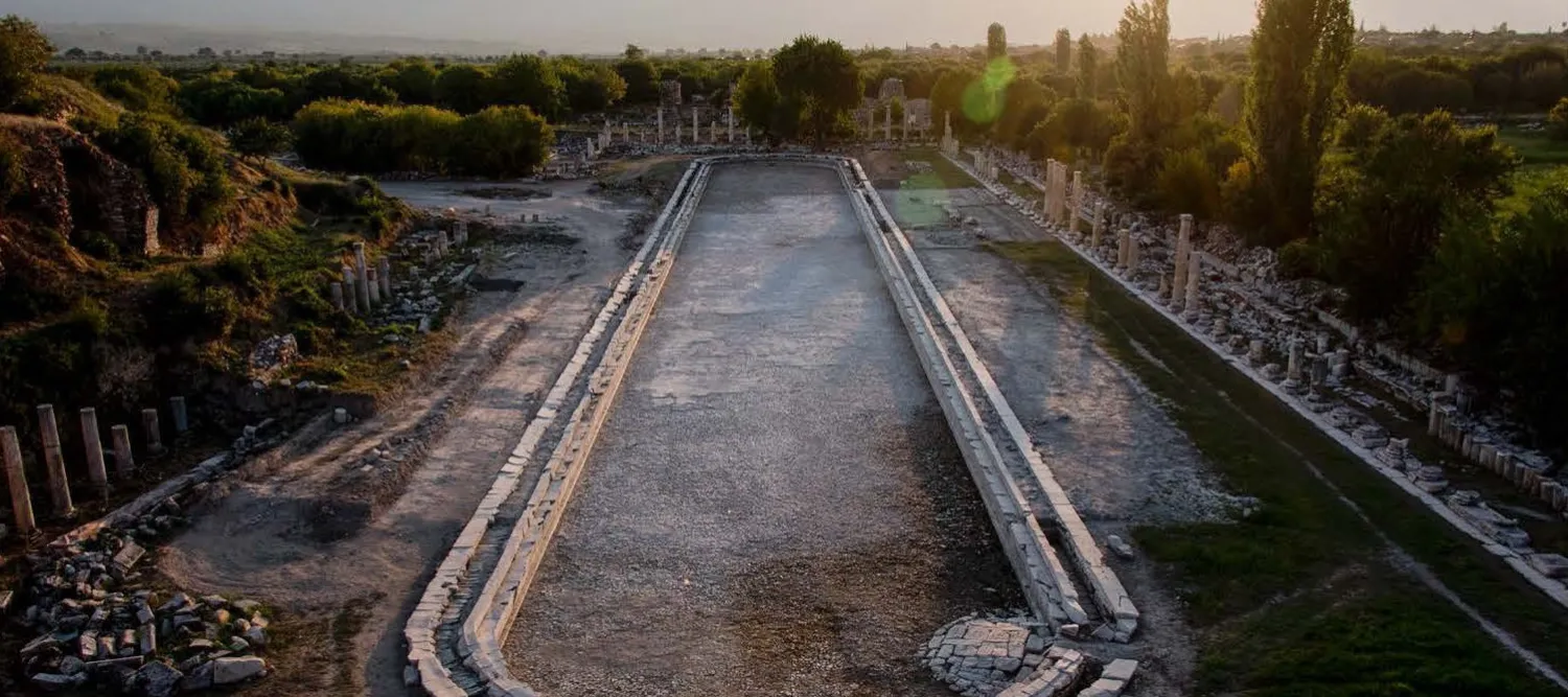 The Place of the Palms at sunset. A large open area, which appears to be the remains of a pool, is fringed with trees.