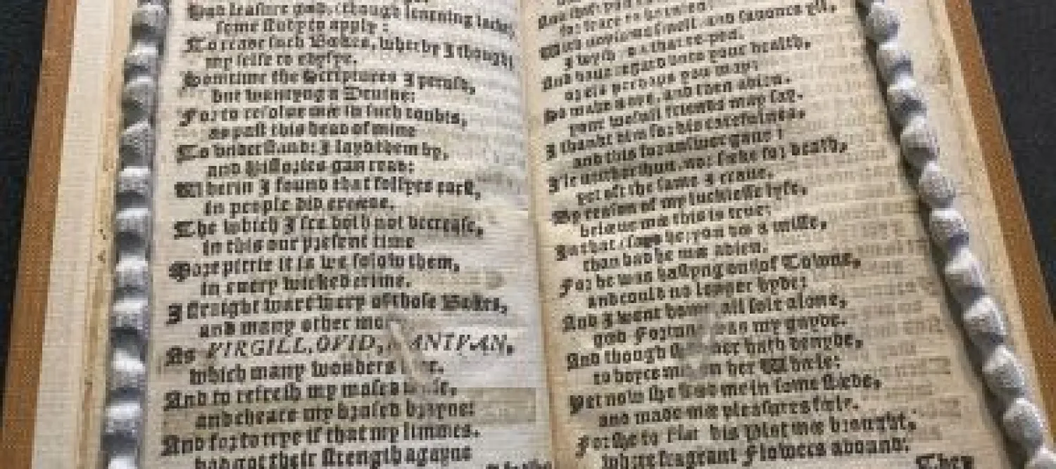 Open antique book with dense blackletter text framed by braided cords.