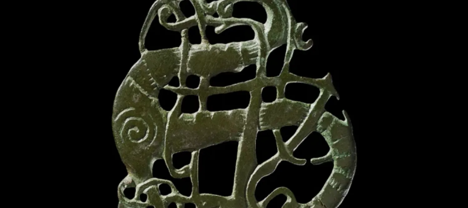 An ancient dark bronze animal-shaped ornament with intricate interlaced curves and cutouts, isolated against black; its weathered surface feels mysterious and archaic.