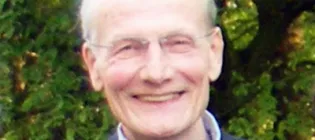Alan Day has short white hair and wears framed glasses. He smiles into the camera.