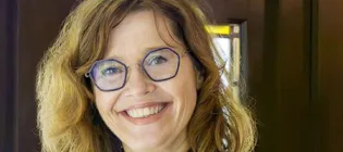 Professor Graziosi wears glasses and a blue shirt and stands beside a window, her face illuminated by natural ight.