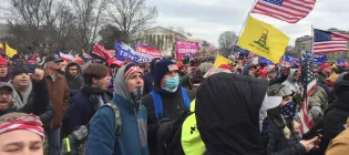 A crowd gathers at the US Capitol building waving American flags.