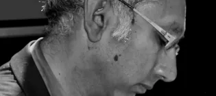Black and white image of Kenan Malik in profile. He has greying hair and wear spectacles.