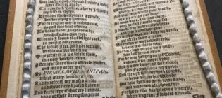 Open antique book with dense blackletter text framed by braided cords.