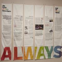 Six cloth banners hang from a wall, the word 'Always' running across the bottom in rainbow-coloured letters.