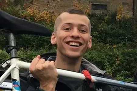 Dominic as a student. He has very short hair and a wide smile. He holds aloft a racing bike.