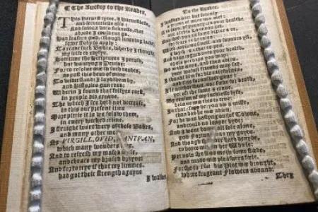 Open antique book with dense blackletter text framed by braided cords.