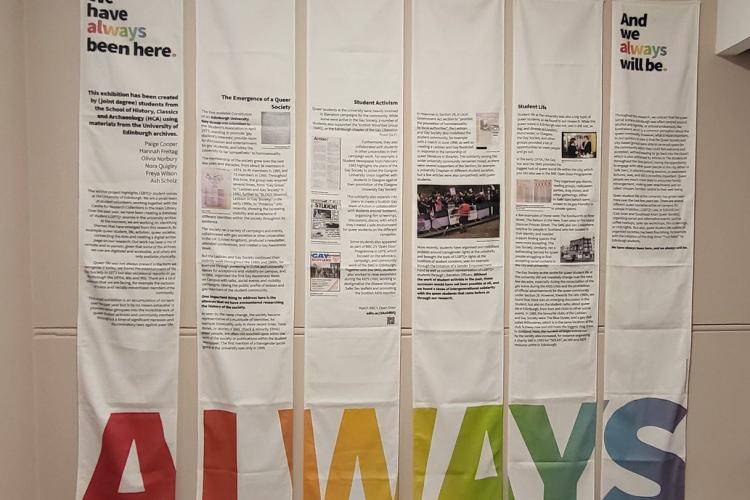 Six cloth banners hang from a wall, the word 'Always' running across the bottom in rainbow-coloured letters.