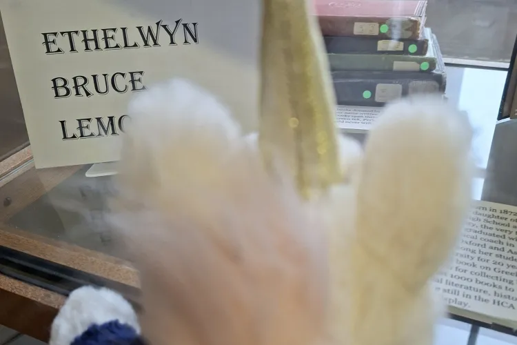 A fluffy unicorn toy wearing a navy sweater looks into a display case about Ethelwyn Bruce Lemon