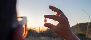 A student holds a flint arrow head between finger and thumb against a sunset.