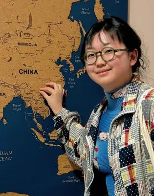 Zhichu has dark hair and wears glasses. They are placing a pin in a map showing where in China they come from.