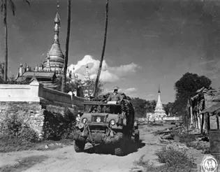 An army jeep drives through a town