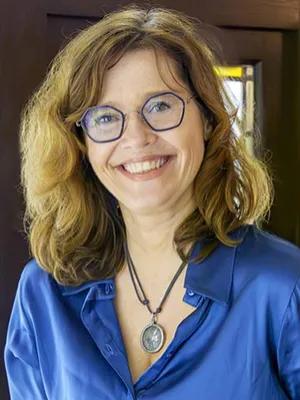 Professor Graziosi wears a blue shirt and glasses and stands in front of a window, with natural light illuminating her face.